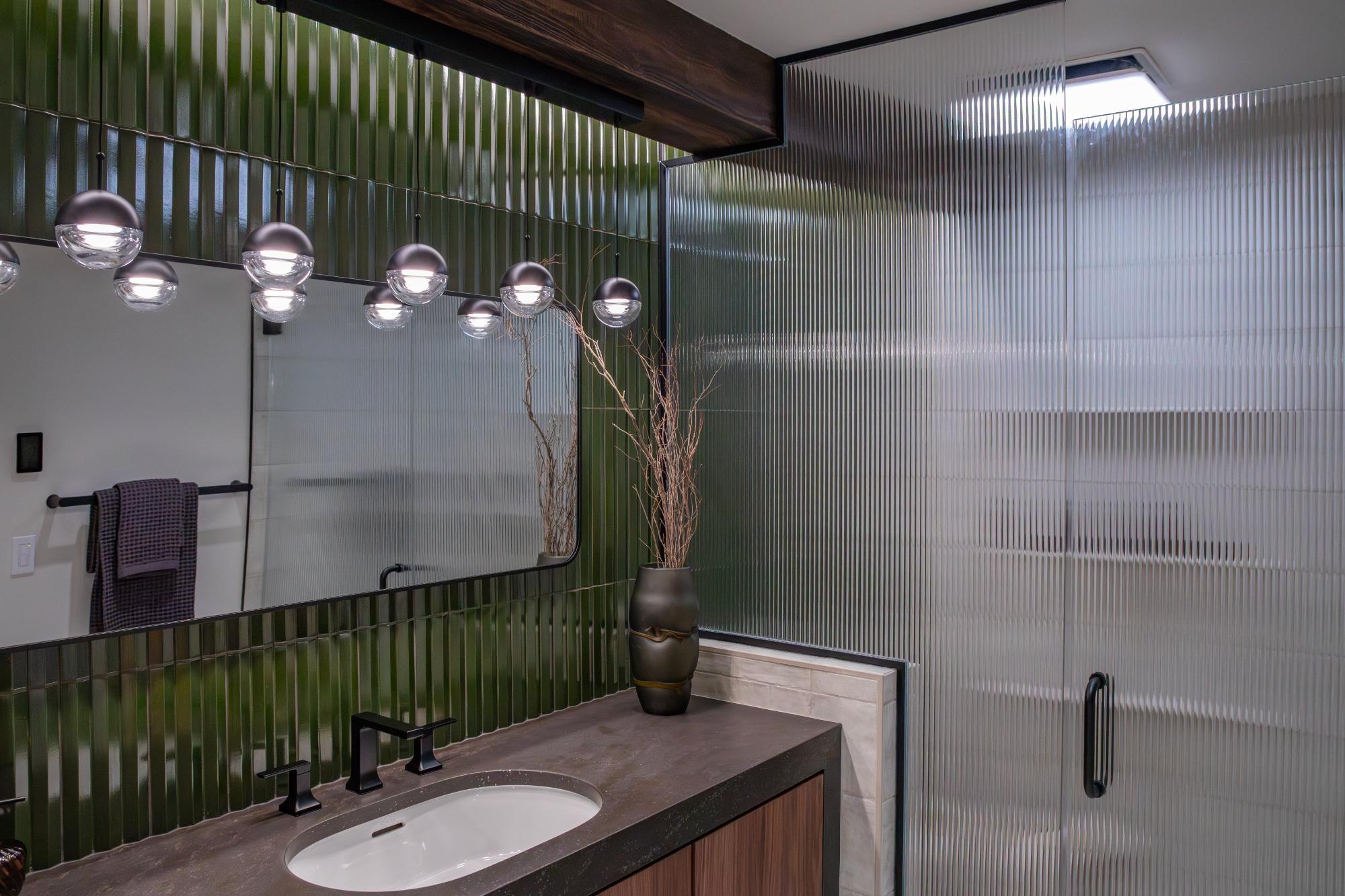 Modern bathroom remodel by HC Remodel & Design in Omaha, NE featuring a ribbed glass shower enclosure, floating vanity, and green tile