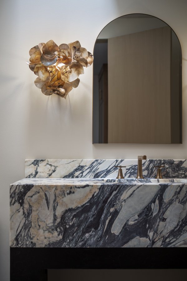 Bathroom remodel by HC Remodel & Design in Omaha, NE featuring a marble waterfall vanity with an arched mirror and designer wall-optimized