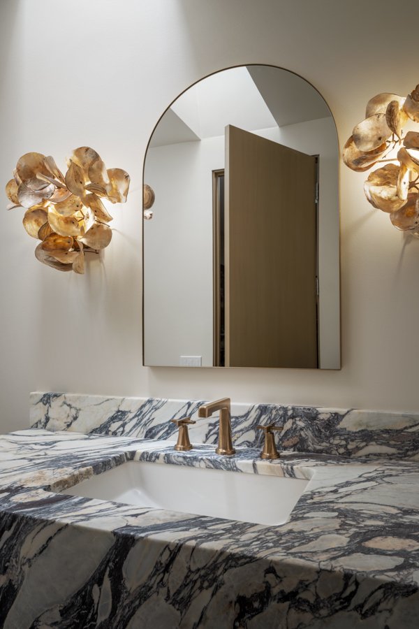 Bathroom remodel by HC Remodel & Design in Omaha, NE featuring an arched mirror above a marble vanity with warm bronze faucet fi-optimized