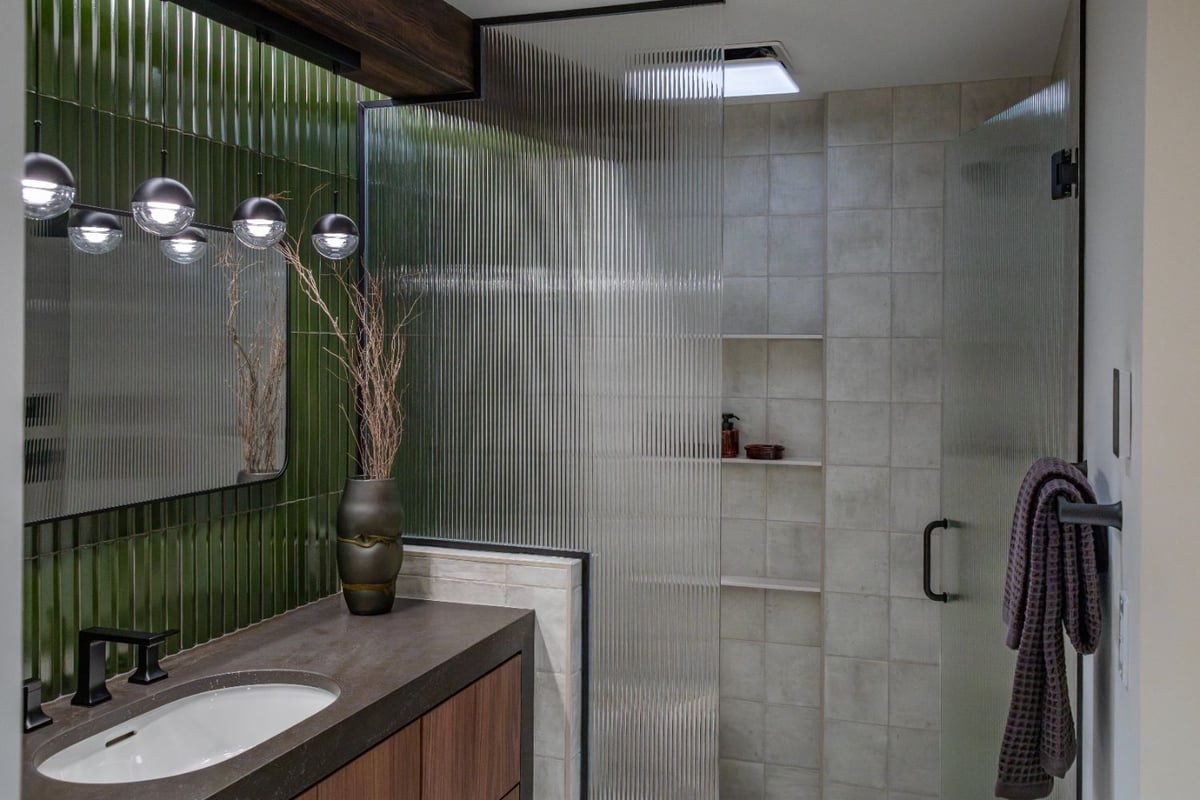 Modern bathroom remodel by HC Remodel & Design in Omaha, NE featuring a walnut vanity, green tile accent wall, and fluted glass -optimized