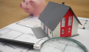 Stock image of a magnifying class, little house, and blueprints