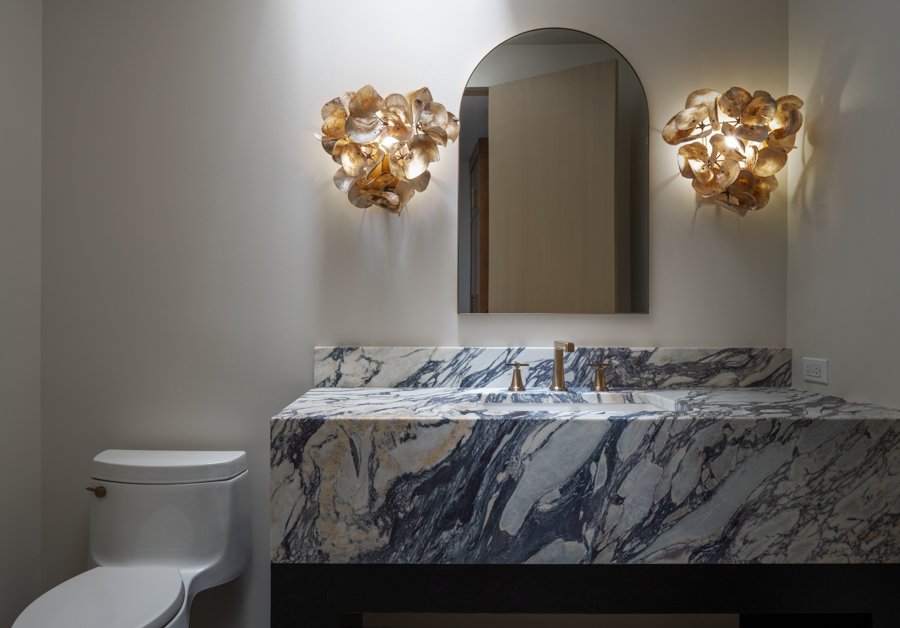 Bathroom remodel by HC Remodel & Design in Omaha, NE with a marble waterfall vanity, arched mirror, decorative sconces, and mode-optimized