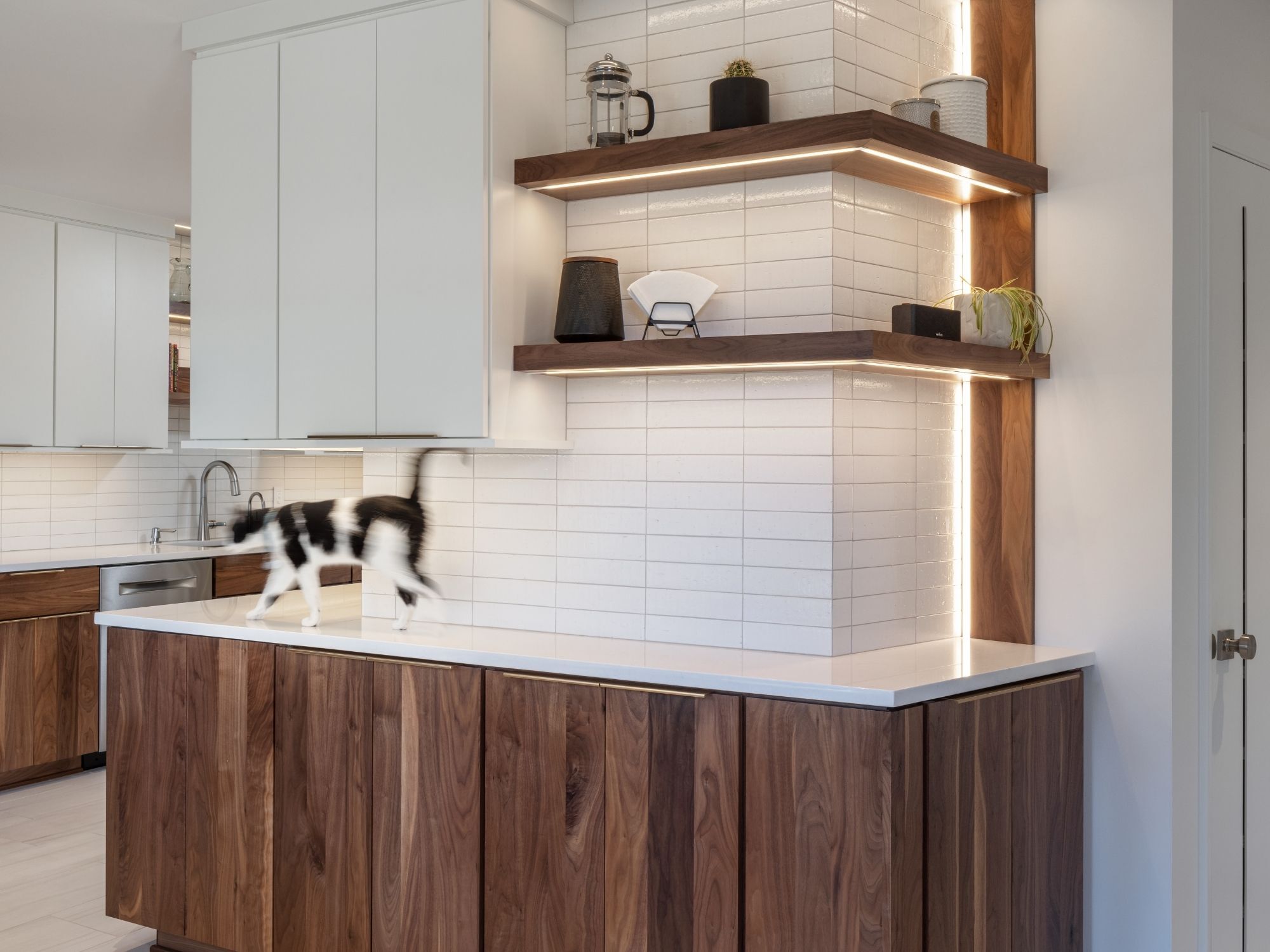 Modern kitchen with walnut cabinetry, illuminated open shelving, and white tile in Omaha & Council Bluffs.